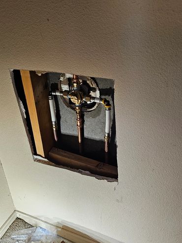 Exposed plumbing behind a wall with tools scattered on the floor.