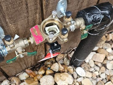 Outdoor gas meter setup with pipes and valves against a wooden fence.