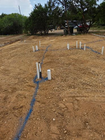 Construction site with plumbing pipes and blue marker lines on dirt ground.