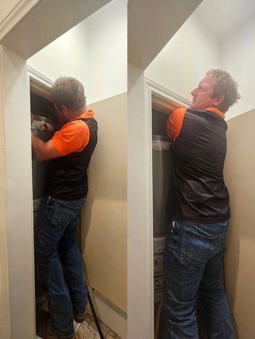 Man wearing orange and black shirt fixing a water heater inside a small closet.