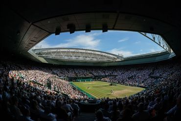 A packed tennis stadium with players competing on a grass court under a blue sky.