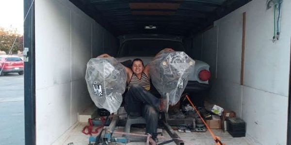 A person sitting inside a trailer with a car and covered engines.