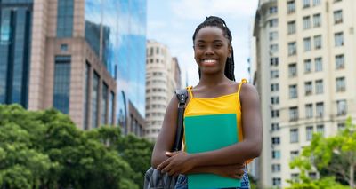Laughing african american young adult female student with dreadlocks outdoor in summer in city