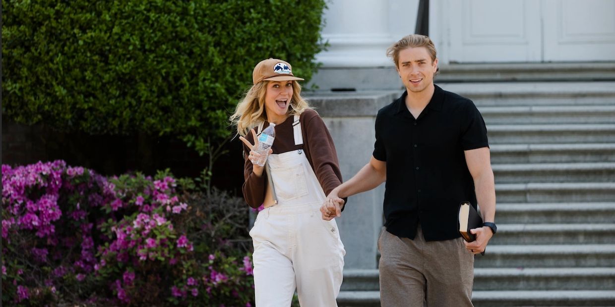 A cheerful couple holds hands walking outdoors near stairs and flowers.