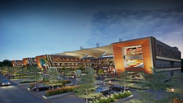 Modern shopping center with illuminated food advertisements and landscaped parking lots at dusk.