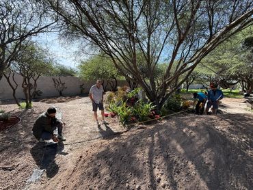 Four men working outdoors measuring a garden area with a tape measure.
