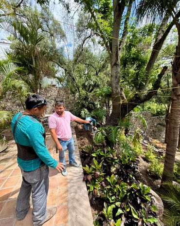 Two men discussing gardening work in a lush outdoor garden area.