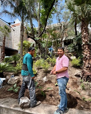 Two men gardening outdoors on a sunny day with trees and plants.