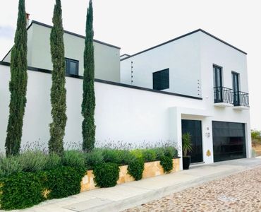 Modern white house with tall cypress trees and black accents.
