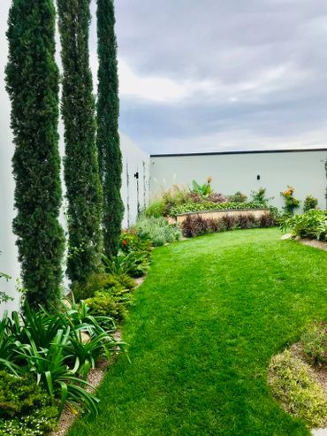 A lush green garden with tall trees and a curved lawn under a cloudy sky.