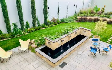 Modern backyard with water feature, greenery, and outdoor seating area.
