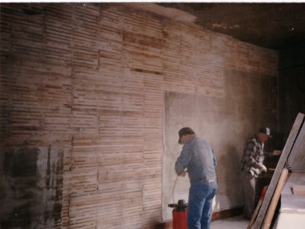 Workers plastering a wall indoors.