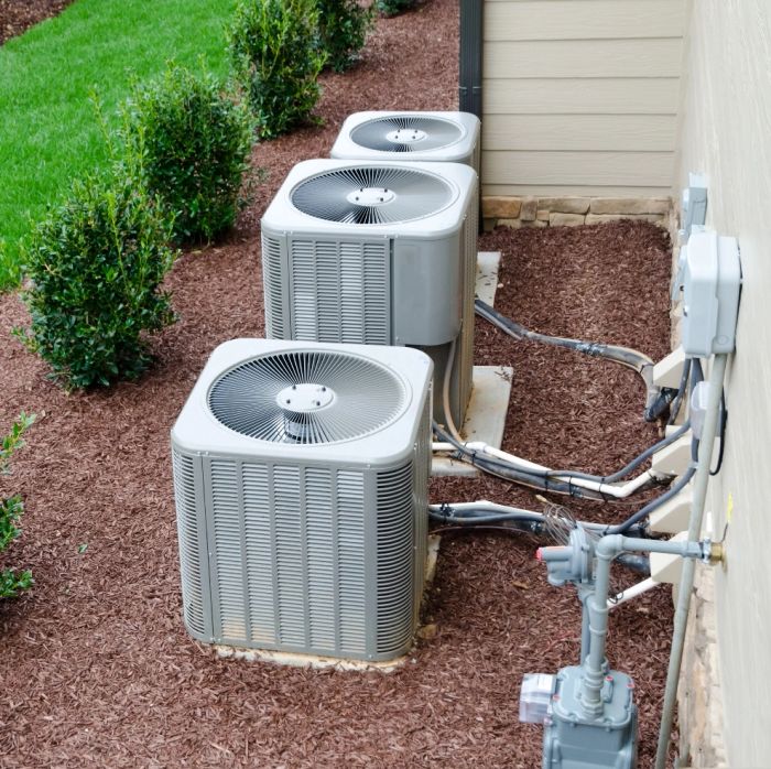 Three outdoor air conditioning units installed beside a house.