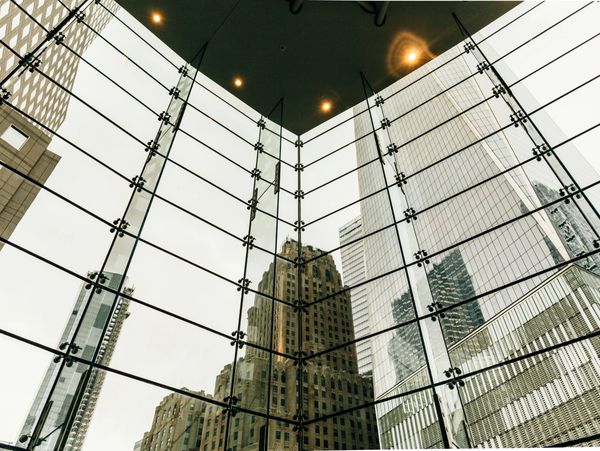 View of city skyscrapers through a glass wall with ceiling lights.
