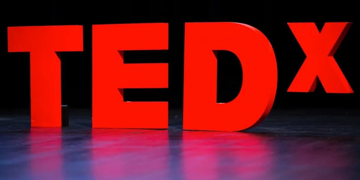 Large red TEDx letters on a stage with a dark background.