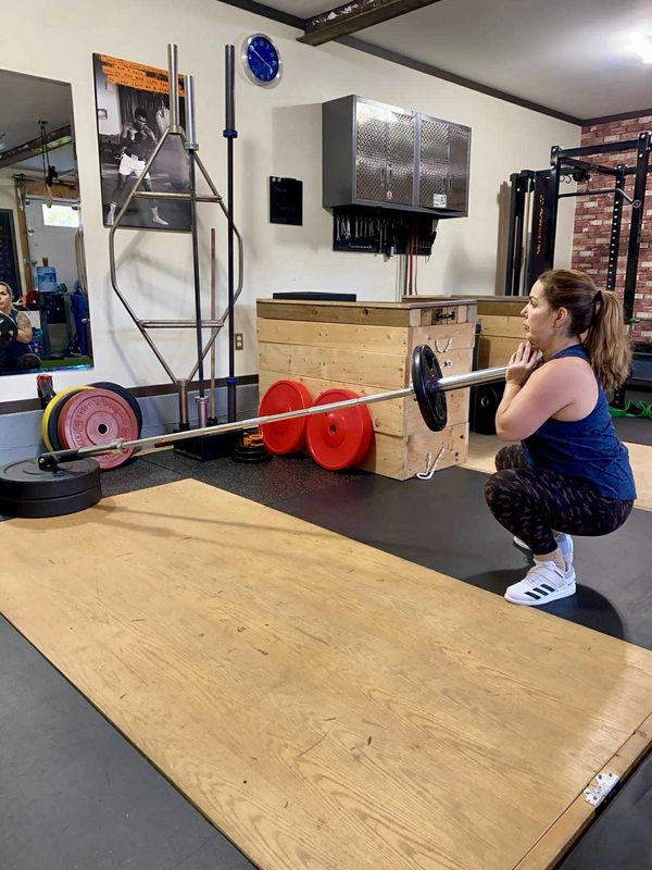 Woman performing a goblet squat with a pole and weights.