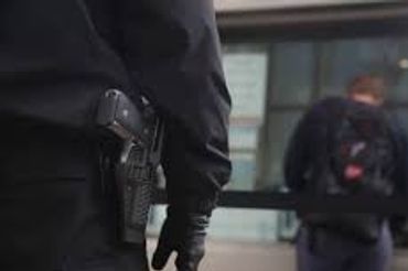 Security guard with a gun monitoring a person walking away.