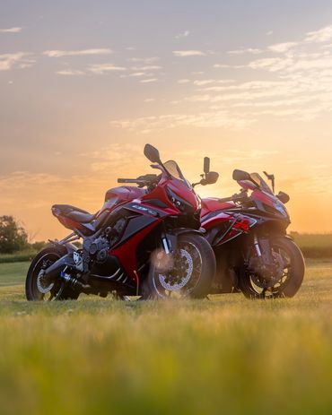 Two red sport motorcycles parked on grass during a golden sunset.