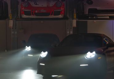 Sports cars with headlights on in a dimly lit garage with elevated platforms.