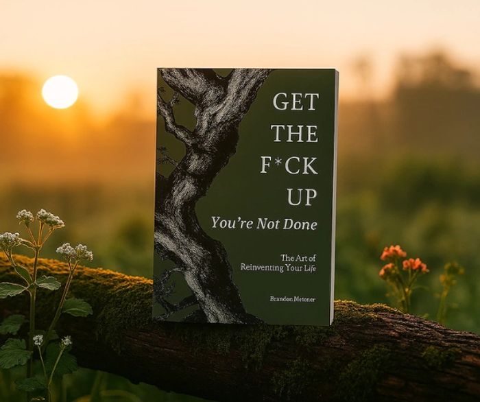 Book titled 'Get The F*ck Up' on a mossy log at sunset.