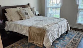 A bed with brown headboard and tan and brown bed set on a wool rug after recurring maid services.