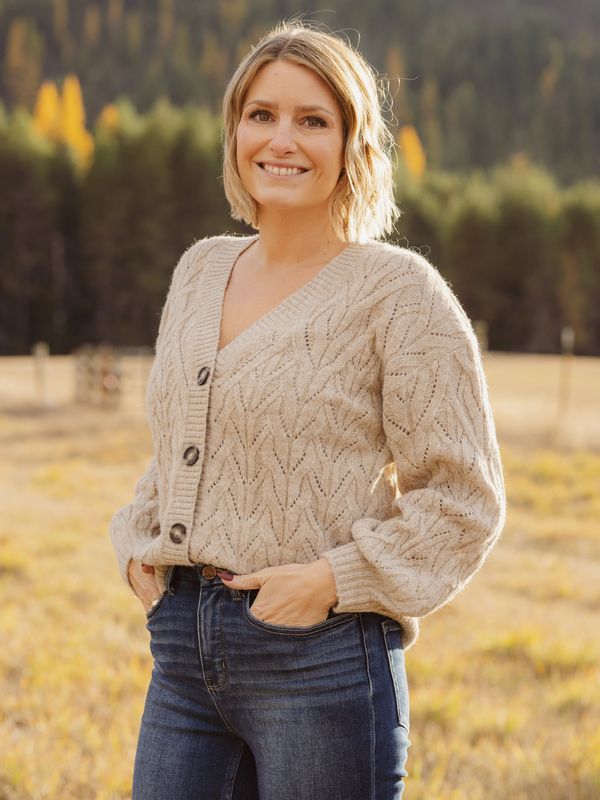 Smiling woman in a beige knitted cardigan and jeans outdoors.