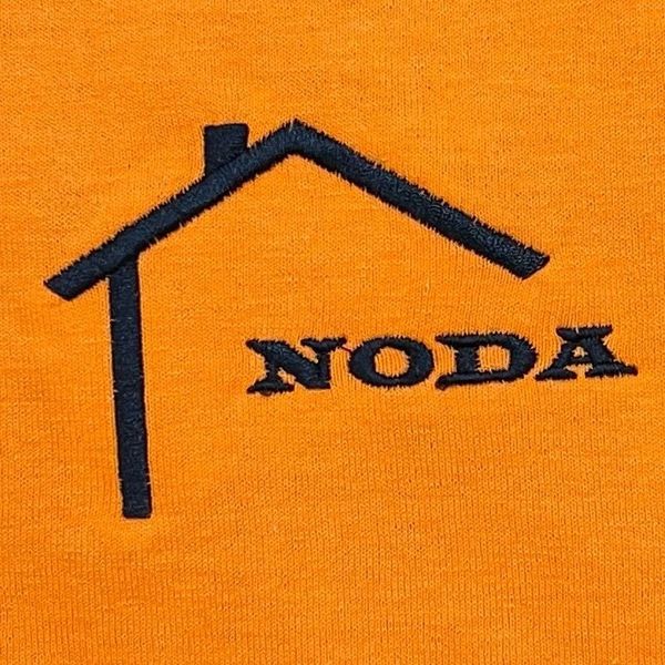 Black embroidered house outline and 'NODA' text on orange fabric.