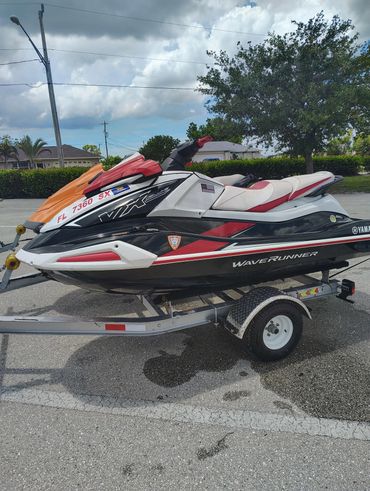 Two Yamaha WaveRunner jet skis on trailers in a parking lot under a cloudy sky.