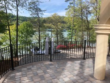 Scenic lakeside patio with stone flooring and black railing under a clear sky.