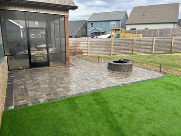 Backyard patio with a fire pit, artificial grass, and a screened porch area.