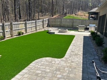 Backyard with artificial turf, stone patio, and outdoor grill area.