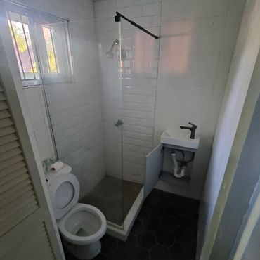 Compact bathroom with toilet, small sink, and glass shower enclosure.