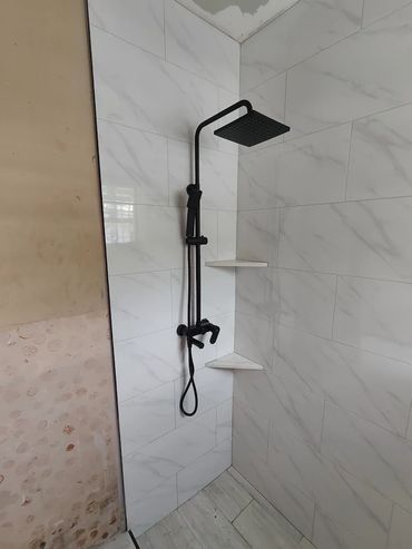 Modern black shower fixture installed on white marble-style tiled wall.