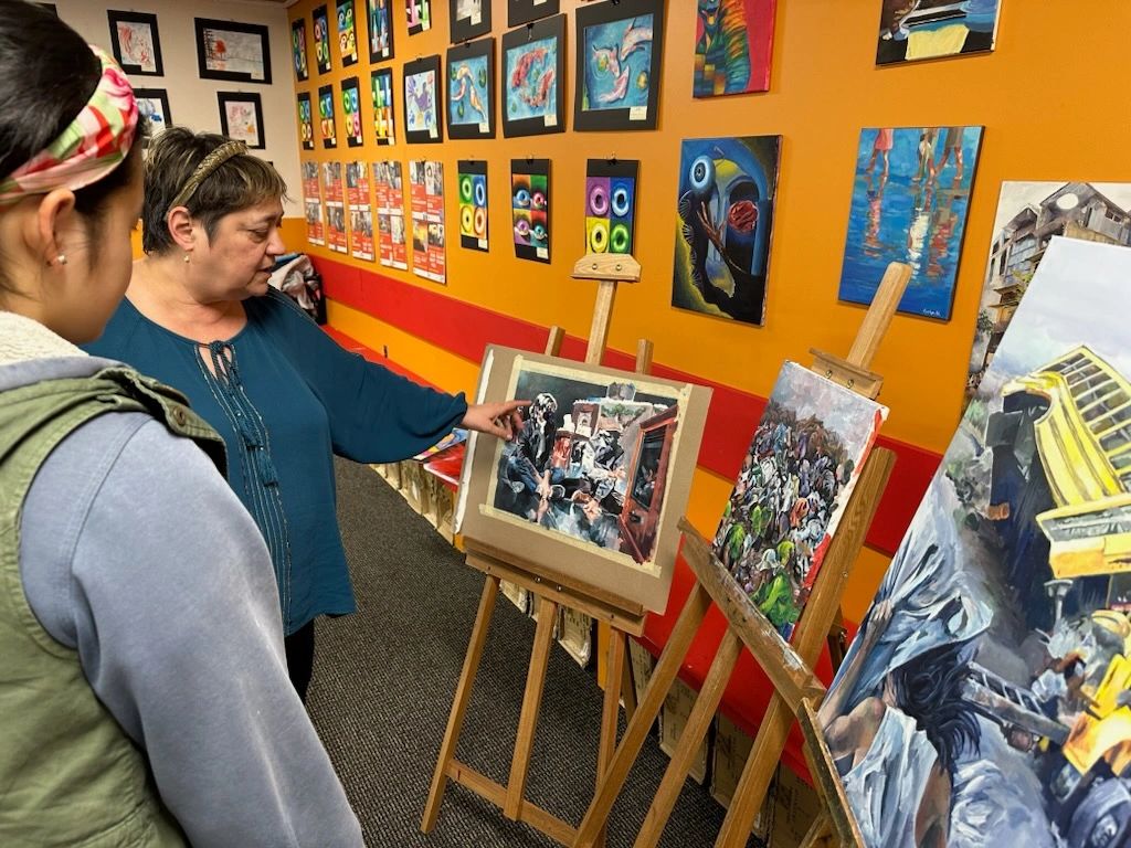 An art teacher explains a painting to a student in a colorful classroom.
