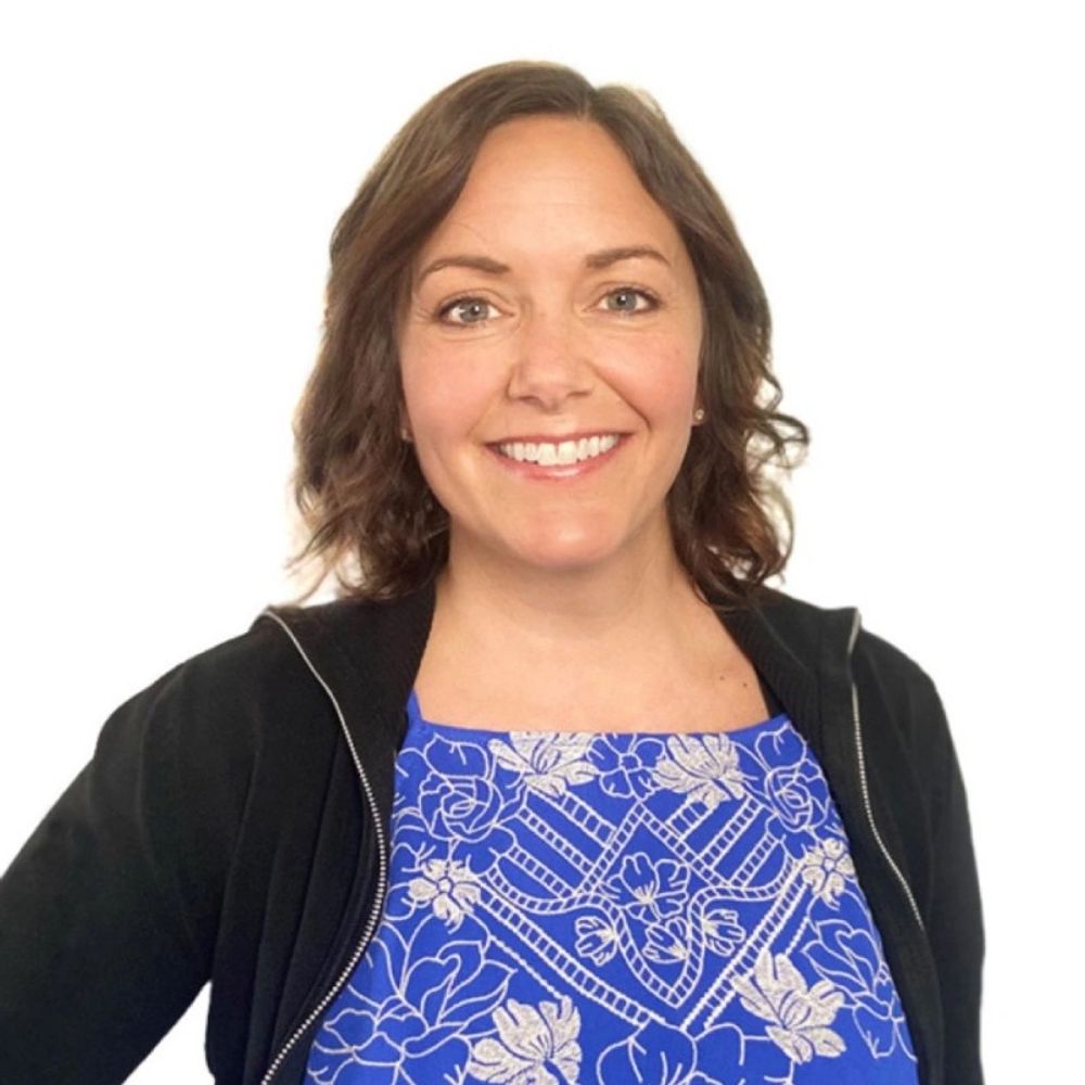 Smiling woman wearing a blue floral dress and black jacket.