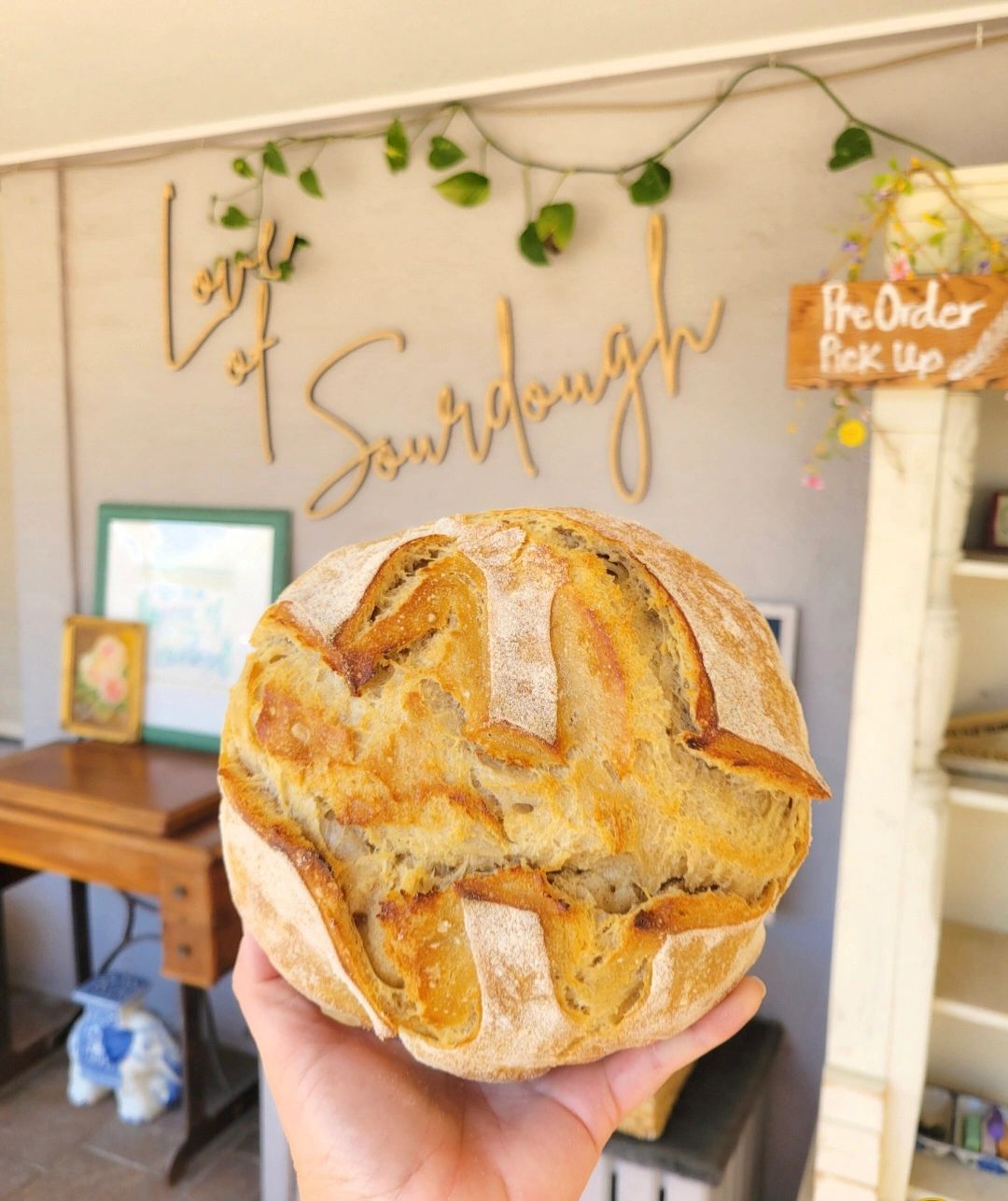 Freshly baked sourdough bread held up in a cozy bakery setting.
