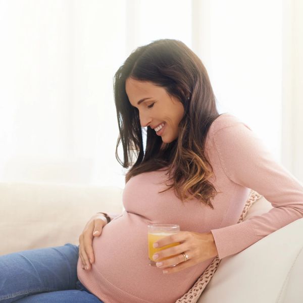 Pregnant woman smiling and holding a glass of juice.
