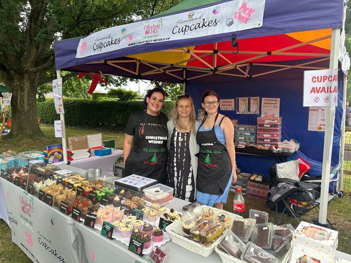 Three women at a colorful cupcake stall with various cupcakes displayed.