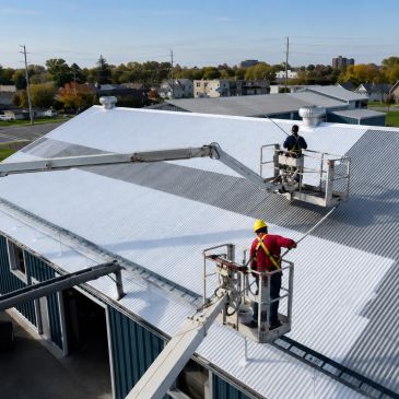 Workers painting a metal roof white using aerial lifts.