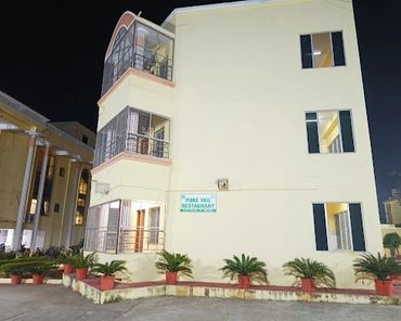 A brightly lit three-story building with a sign for a pure vegetarian restaurant at night.