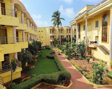 Yellow residential buildings surrounding a lush green courtyard with palm trees.