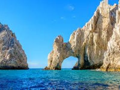 Natural rock arch formation by the sea under a clear blue sky.