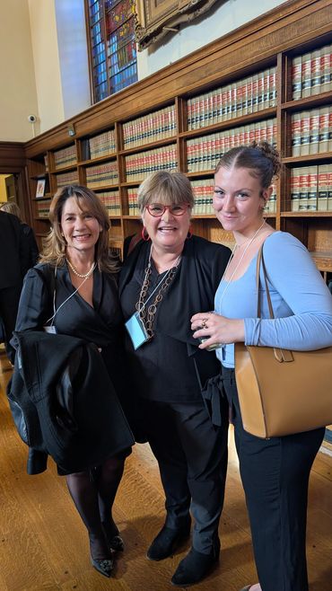 Three women smiling together in a library with shelves of law books behind them.