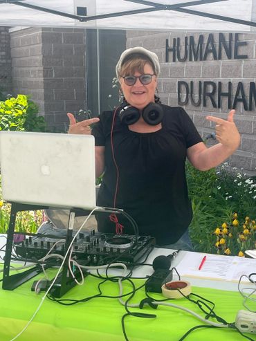 Woman DJing outdoors with headphones and equipment at Humane Durham event.