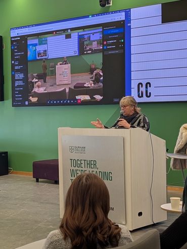 Speaker addressing an audience at Durham College in a modern conference room.
