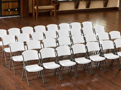 Rows of white folding chairs on wooden floor.