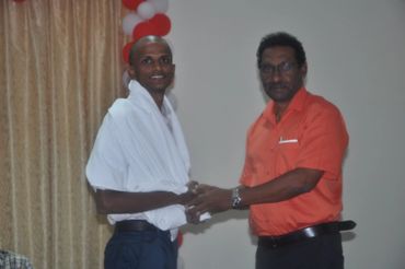 Two men shaking hands during a formal event with red and white balloons.