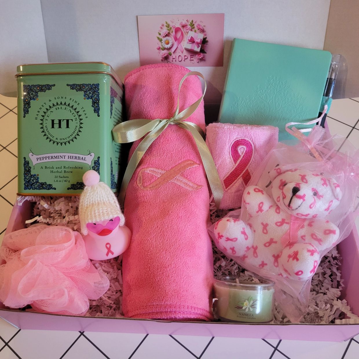 Breast cancer awareness gift box with pink-themed items and a green tea tin. Gifts that delight!