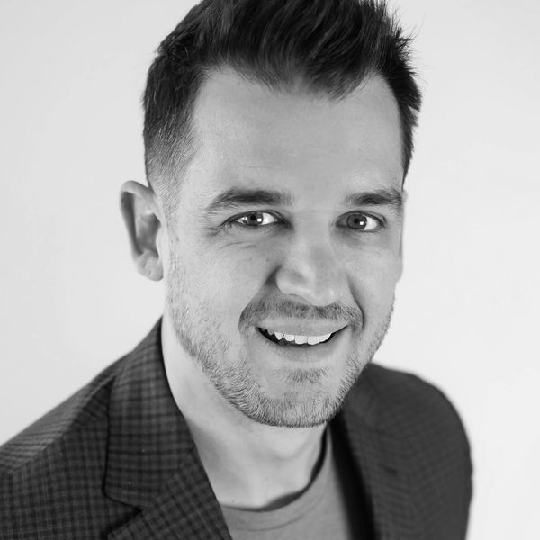Smiling man with short dark hair wearing a checkered blazer and gray shirt.