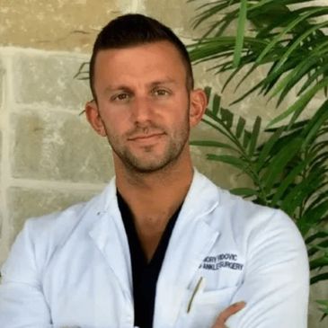 A confident male doctor in a white coat posing with arms crossed.